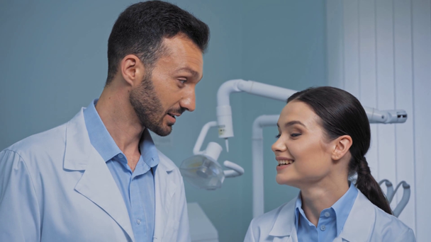 Χαμογελώντας οδοντίατροι σε λευκές ποδιές μιλώντας στην κλινική  - Πλάνα, βίντεο