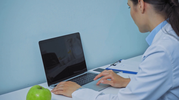 Zubař pomocí notebooku v blízkosti jablka a schránky na stole - Záběry, video