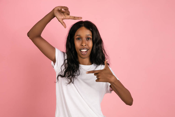 Cheerful african-american young woman isolated on pink background, emotional and expressive - 写真・画像