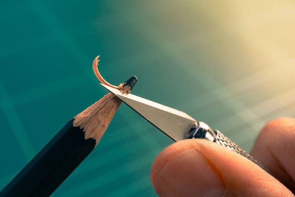 Μακρο εικόνα του χεριού ακόνισμα αμβλύ μολύβι με μαχαίρι τέχνης σε πράσινο στρώμα κοπής. δοκιμαζόμενη ιδέα - Φωτογραφία, εικόνα