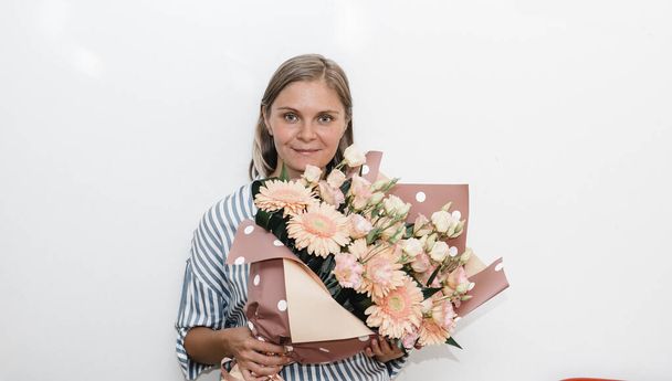 jeune femme en chemisier bleu rayé tient un énorme bouquet de fleurs de gerbera rose orange. cadeau d'anniversaire à la femme.  - Photo, image
