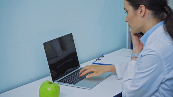 Dentista utilizzando il computer portatile e parlando su smartphone in clinica - Filmati, video