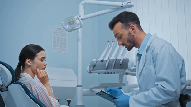 Όμορφος γιατρός με πρόχειρο μιλάει με ασθενή στην κλινική  - Πλάνα, βίντεο