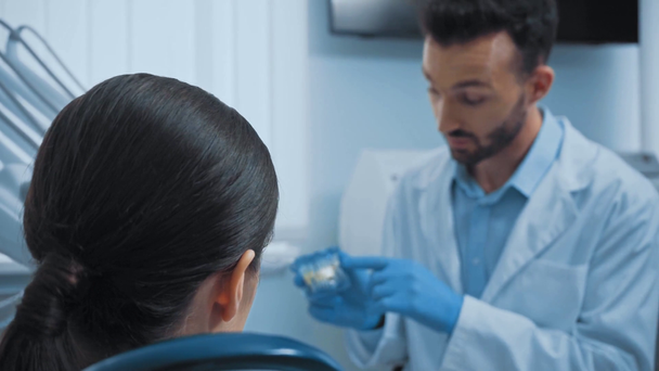 Οδοντίατρος σε γάντια λατέξ που δείχνει το μοντέλο των δοντιών στον ασθενή στην κλινική  - Πλάνα, βίντεο