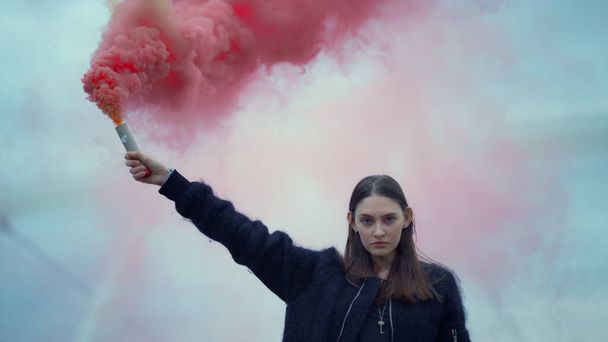 Mujer parada en la calle con una bomba de humo en la mano. Chica sosteniendo granada de humo
 - Foto, Imagen