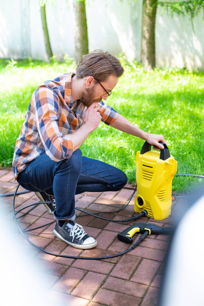 Young man in casual clothes, using a high pressure washer in the garden. - Foto, imagen
