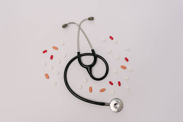 Stock photo of a stethoscope surrounded by different pills on a white background. There is nobody on the picture. - Photo, Image