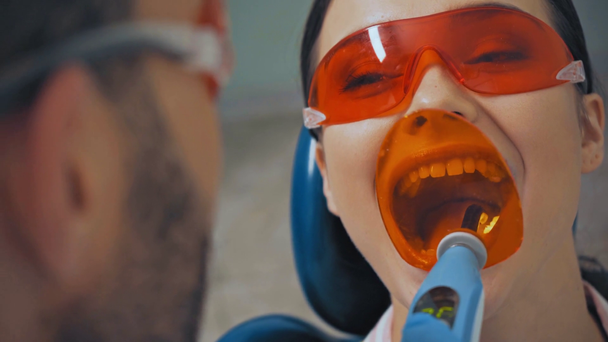 Γιατρός που χρησιμοποιεί φως οδοντιατρικής θεραπείας ενώ εργάζεται με τον ασθενή με γυαλιά ασφαλείας  - Πλάνα, βίντεο