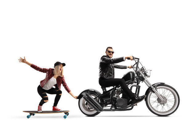 Full length profile shot of a biker riding a chopper and pulling a female on a skateboard isolated on white background - Foto, immagini