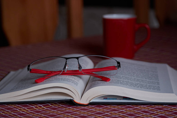 Intellektuelles Unterhaltungskonzept. Buch mit leerem Einband neben roten Gläsern, Kaffee auf einem Tisch. - Foto, Bild