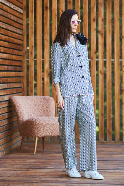 Young woman in pajamas is standing on wooden terrace in tropical country and look on jungle - 写真・画像