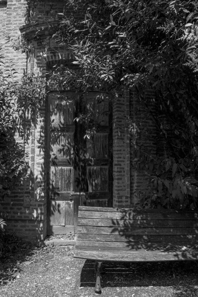 Стара лавка під деревом перед дверима стародавнього будинку. Дерев'яна лавка перед цегляною віллою, покритою старою рослиною
. - Фото, зображення
