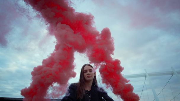 Girl posing at camera in colorful smoke. Attractive woman holding smoke bombs - Photo, Image