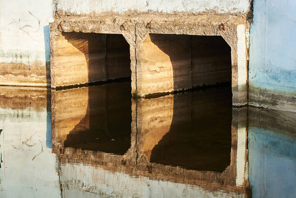 人工貯水池からの水の放出のための出口コレクターは、水に反映されます - 写真・画像