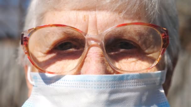 Detail portret van oma in beschermende masker van virus. Oudere vrouw die in de camera kijkt met scherp zicht. Concept van gezondheid en veiligheid als gevolg van een pandemie. Quarantaine van het coronavirus voor ouderen - Video