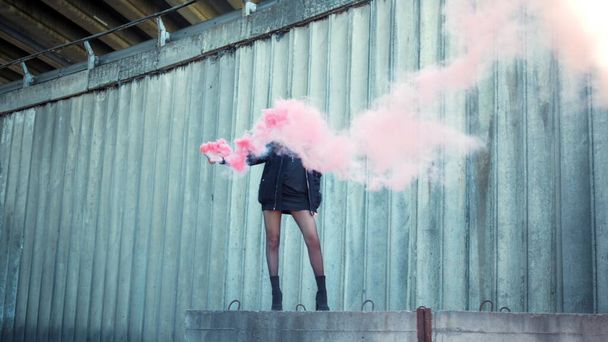 Girl standing on street with smoke bomb in hand. Woman holding smoke grenade - Foto, Imagen