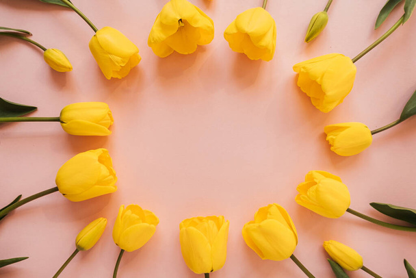 Kulatý rám věnec s prázdným kopírovacím prostorem ze žlutých tulipánových květin na růžovém pozadí. Flat lay, top view květinový sváteční koncept - Fotografie, Obrázek