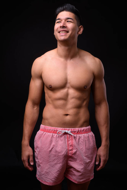 Studio shot of young handsome muscular multi ethnic man shirtless against black background - Photo, image