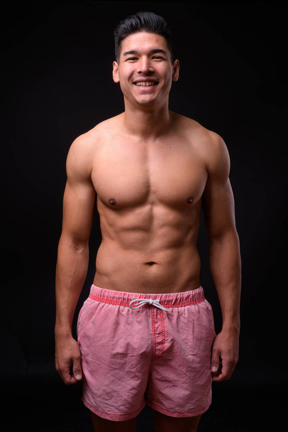 Studio shot of young handsome muscular multi ethnic man shirtless against black background - Photo, image