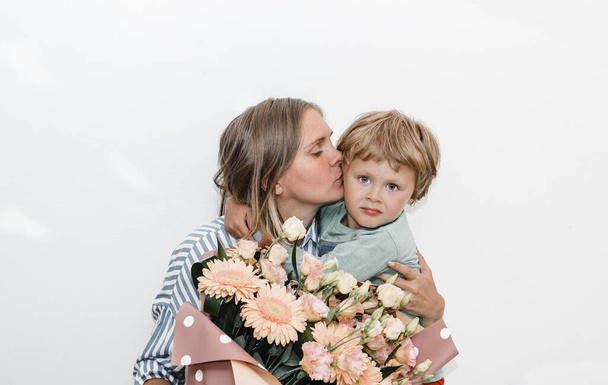 Sohn und junge Mutter umarmen und küssen sich. das Kind gratulierte seiner Mutter zum Geburtstag und übergab Blumenstrauß  - Foto, Bild