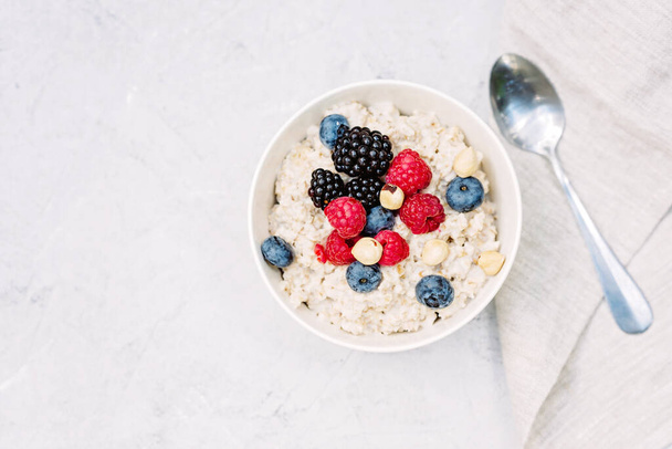 Oatmeal with raspberries, blueberries, blackberries and nuts on a gray concrete background. Healthy healthy breakfast. Flat lay - Foto, imagen
