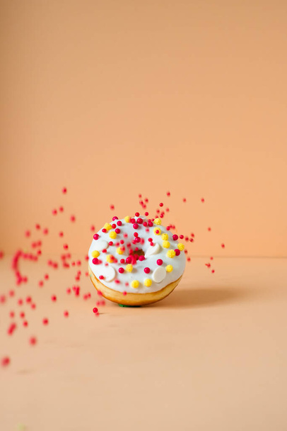 donut met witte glazuur en vliegende rode ballen geïsoleerd op perzik achtergrond  - Foto, afbeelding
