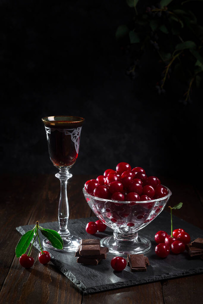 Licor de cereza en una copa con chocolate y cerezas sobre un fondo oscuro. - Foto, Imagen