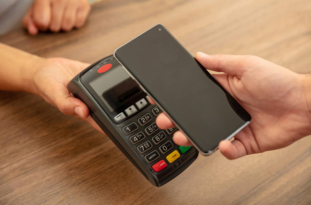 Mobile payment, smart phone nfc, near field communication wireless technology. Cashier and customer hands with POS machine and smartphone, closeup view - Photo, Image