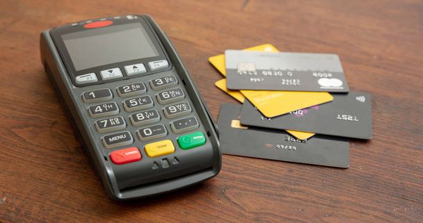 木製の背景にPOS端末とクレジットカード、非接触支払いのためのターミナルレジマシン。銀行機器、消費者主義、ショッピングコンセプト - 写真・画像