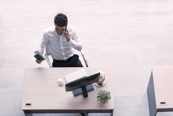 Widok kierownika, menedżera lub inżyniera pijącego sok kokosowy pracującego na komputerze przy użyciu smartfona w biurze kreatywnym na odległość społeczną. - Zdjęcie, obraz