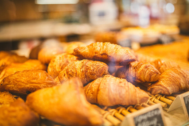 Croissants in the showcase at bakery. Close up of beautiful appetizing golden croissants in cafe on shop window. Assortment of delicious and buttery croissants made by pastry chef. Natural light. - Foto, imagen