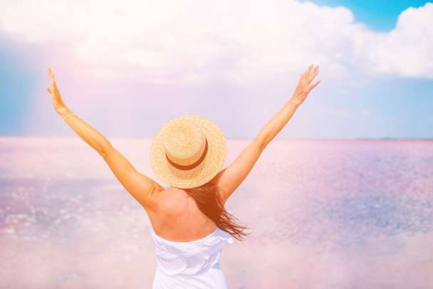 夏の晴れた日にピンク色の塩湖を歩く帽子の女性. - 写真・画像