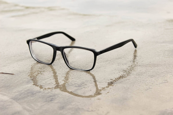 Glasses with diopters lie on the wet sand on the beach. Close-up, selective focus. - Photo, Image