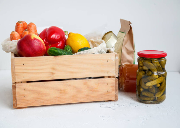 Canned food, cereals, fruits, different vegetables on a white background. Donation wooden box with various food. - Fotó, kép