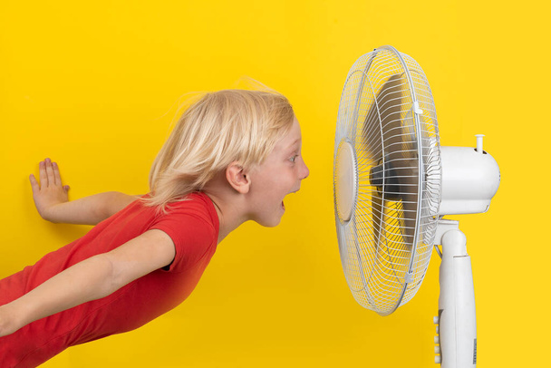 Cheerful boy with blower relaxing. Kid and fan on yellow background. Summer heat. - Photo, Image
