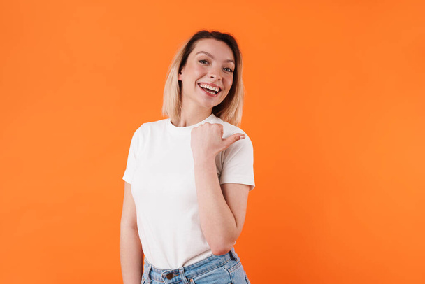 Image of beautiful cheerful woman smiling and pointing finger aside isolated over orange background - Zdjęcie, obraz