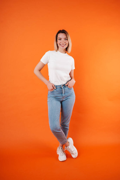 Image of pleased attractive woman smiling and looking at camera isolated over orange background - Fotó, kép