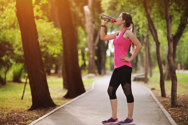 Hermosa atleta de fitness corredor mujer beber agua en el parque. Retrato de una joven sosteniendo una botella de agua en verano. Bosque
 - Foto, Imagen