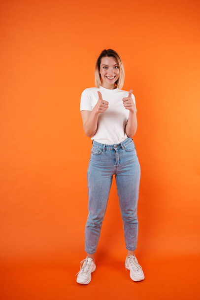 Image of joyful attractive woman smiling and showing thumbs up isolated over orange background - Zdjęcie, obraz
