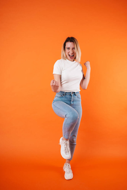 Image of excited attractive woman smiling and making winner gesture isolated over orange background - Фото, зображення