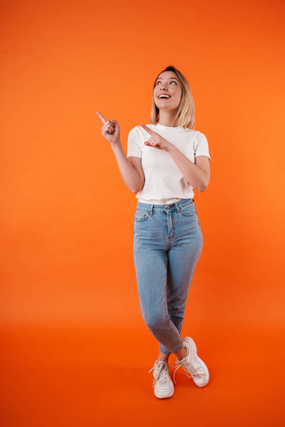 Image of joyful attractive woman smiling while pointing fingers aside isolated over orange background - Fotó, kép