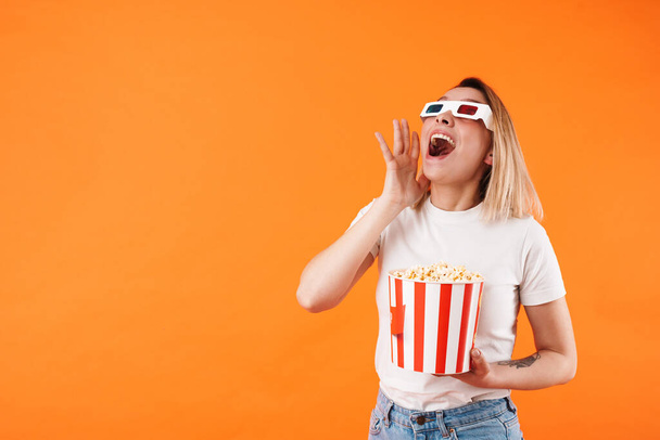 Image of excited woman in 3d glasses watching movie and eating popcorn isolated over orange background - Foto, Imagem
