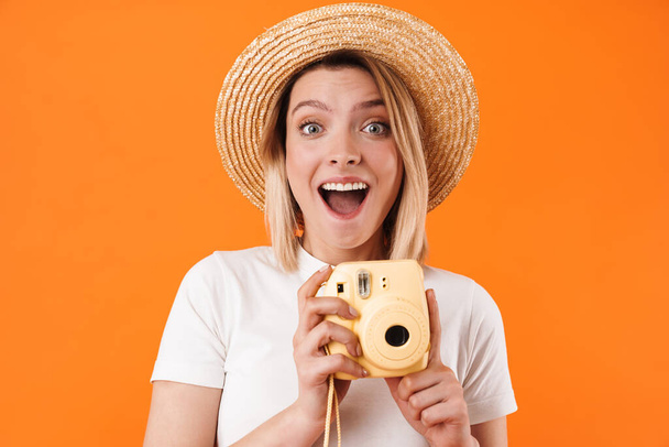 Portrait of lovely cheerful young blonde woman wearing casual clothes standing isolated over orange background, holding instant photo camera - Foto, immagini