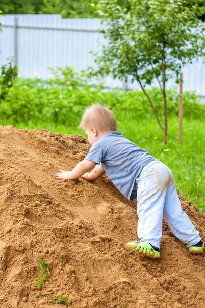 A little boy climbs a mountain with sand. The child is all dirty, but happy. Summer. - Fotó, kép