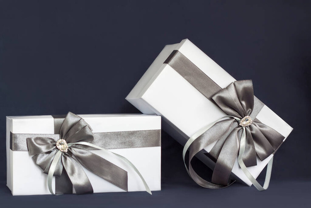 The gift box is white with a beautiful gray bow. Gift on a dark background. Holidays and surprises. Satin bows with rhinestones. - 写真・画像