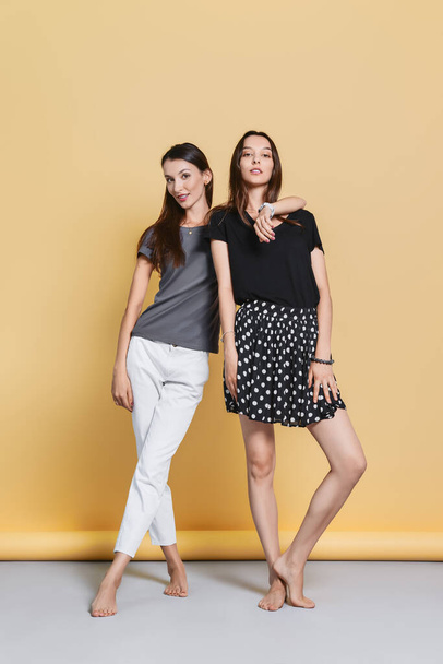 Two happy sisters in casual clothes posing on yellow background - Fotoğraf, Görsel