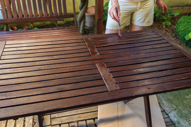 Η γυναίκα ζωγραφίζει ένα παλιό ξύλινο τραπέζι στον κήπο. Κάν 'το μόνος σου. - Φωτογραφία, εικόνα