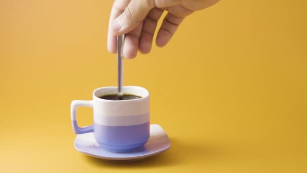 hand stirring coffee on orange background - Filmati, video