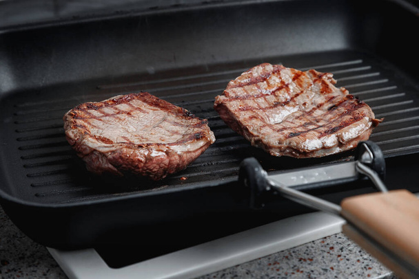 A large piece of fresh beef meat cooked in a grill pan. Stripes on the meat. Fluted frying pan. - Fotoğraf, Görsel