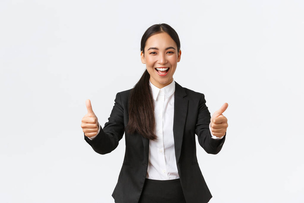 Başarılı iyimser Asyalı iş kadını başparmağını kaldırıyor ve mutlu gülümsüyor. Takım elbiseli neşeli bayan yönetici sevinçle seviniyor iyi haber, iyi iş, iyi iş ya da tebrik jesti deyin - Fotoğraf, Görsel